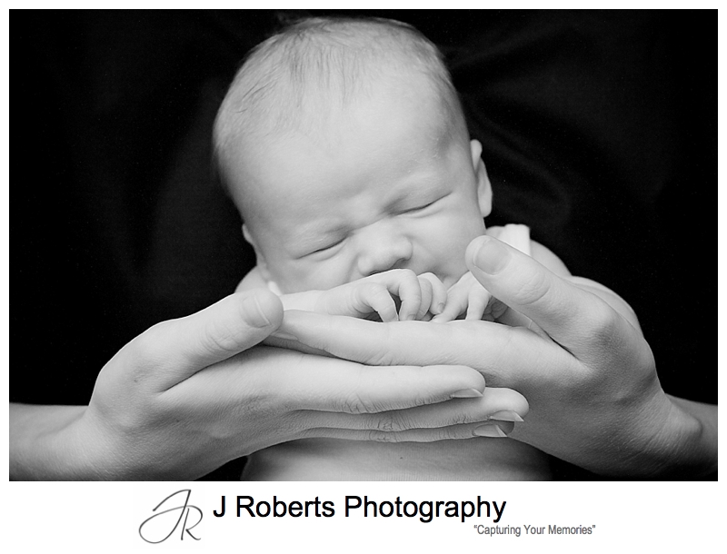 Black and white photo of a sleeping baby in his mothers hands- sydney baby portrait photographer